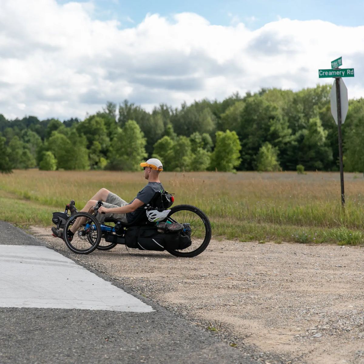 A man rides a Gran Tourismo loaded with panniers on a gravel road in a country setting.