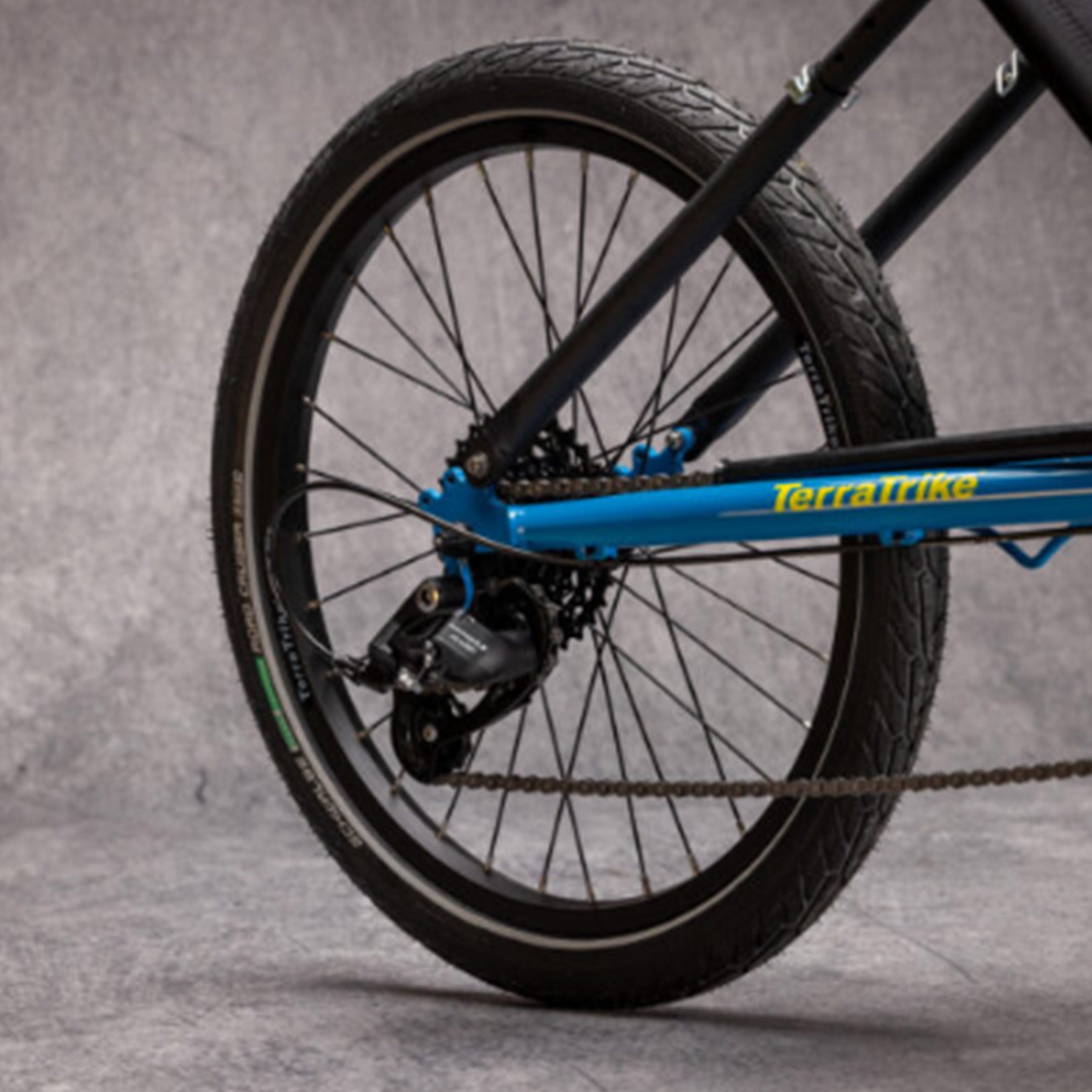 Closeup view of the rear wheel on the TerraTrike Maverick Eiffel Blue Recumbent Trike against a grey background.