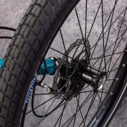 Close-up view of the front wheel on the TerraTrike Rambler E-Plus Recumbent Trike in Gemstone against a grey background.
