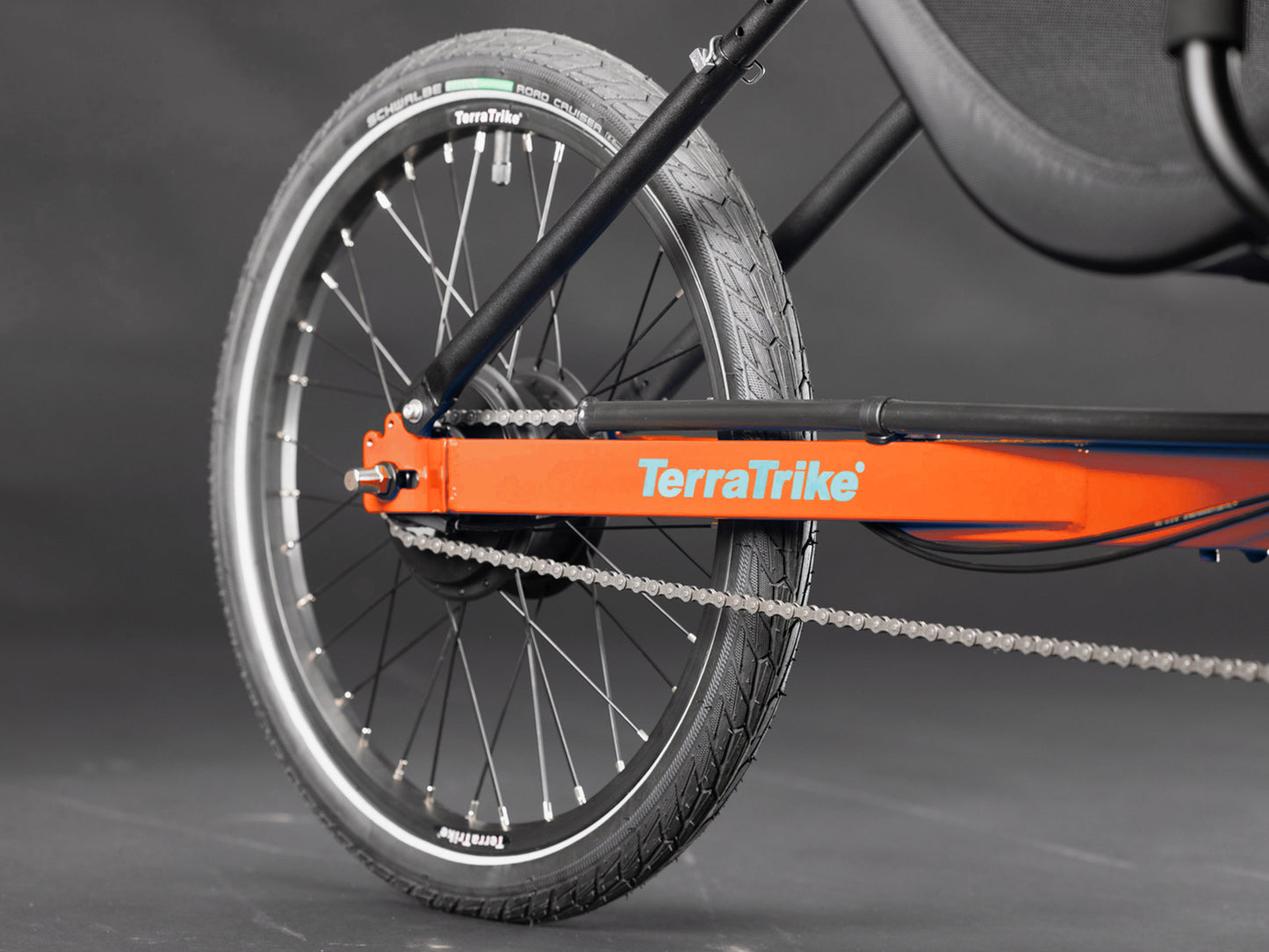 Closeup view of the rear wheel on the TerraTrike Rover Tandem Recumbent Trike in Habanero Orange against a grey background.