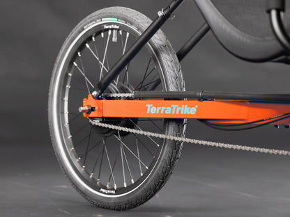Closeup view of the rear wheel on the TerraTrike Rover Tandem Recumbent Trike in Habanero Orange against a grey background.