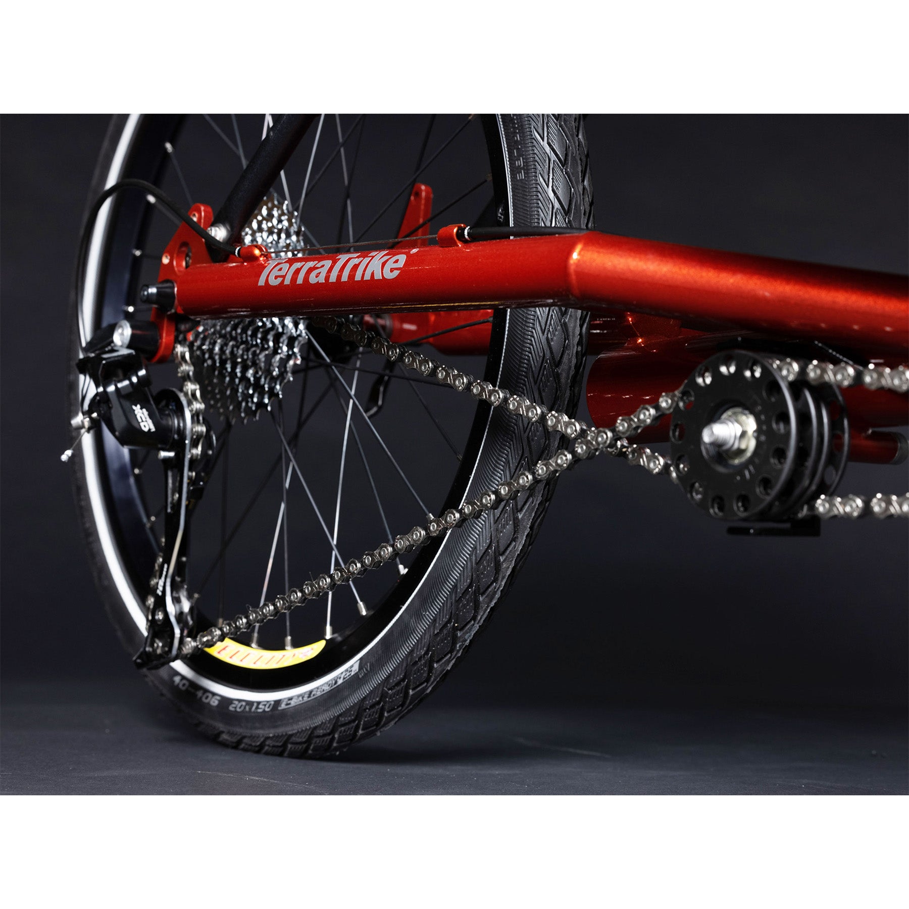 Closeup view of the rear wheel and idler on the TerraTrike Tandem Pro Sparkle Copper Recumbent Trike against a grey background.