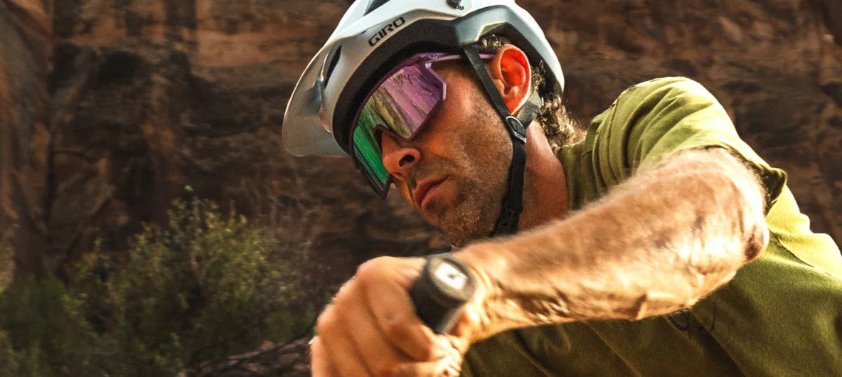 Person wearing a helmet and plum passion Tifosi Moab sunglasses, while riding a bike in a natural setting.