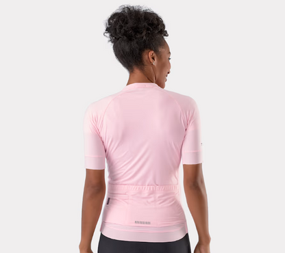 A woman shown from the back wearing a light pink short-sleeve Trek Circuit cycling jersey, paired with black shorts, against a solid light gray background.