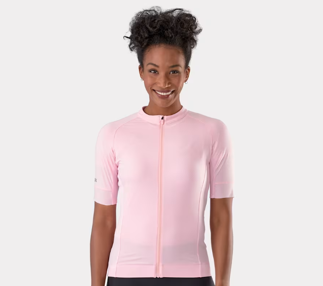 A woman wearing a light pink short-sleeve Trek Circuit cycling jersey with a full front zipper, photographed against a clean light gray studio background.