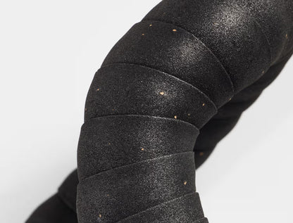 Close up of Trek black gel cork bicycle handlebar tape installed on a handlebar on a white background.