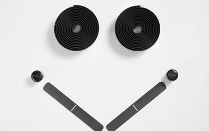 Two rolls of black Trek gel cork bicycle handlebar tape, two black bar end plugs, and two strips of Trek branded finishing tape on a white background.