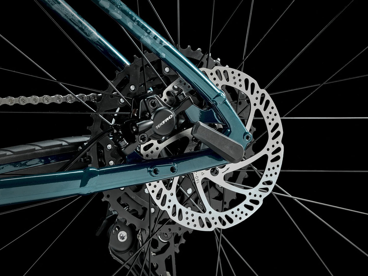A closeup view of the rear disc brake of the Trek Marlin 6 Gen 3 mountain bike in Miami Green to Dark Aquatic Fade against a black background.