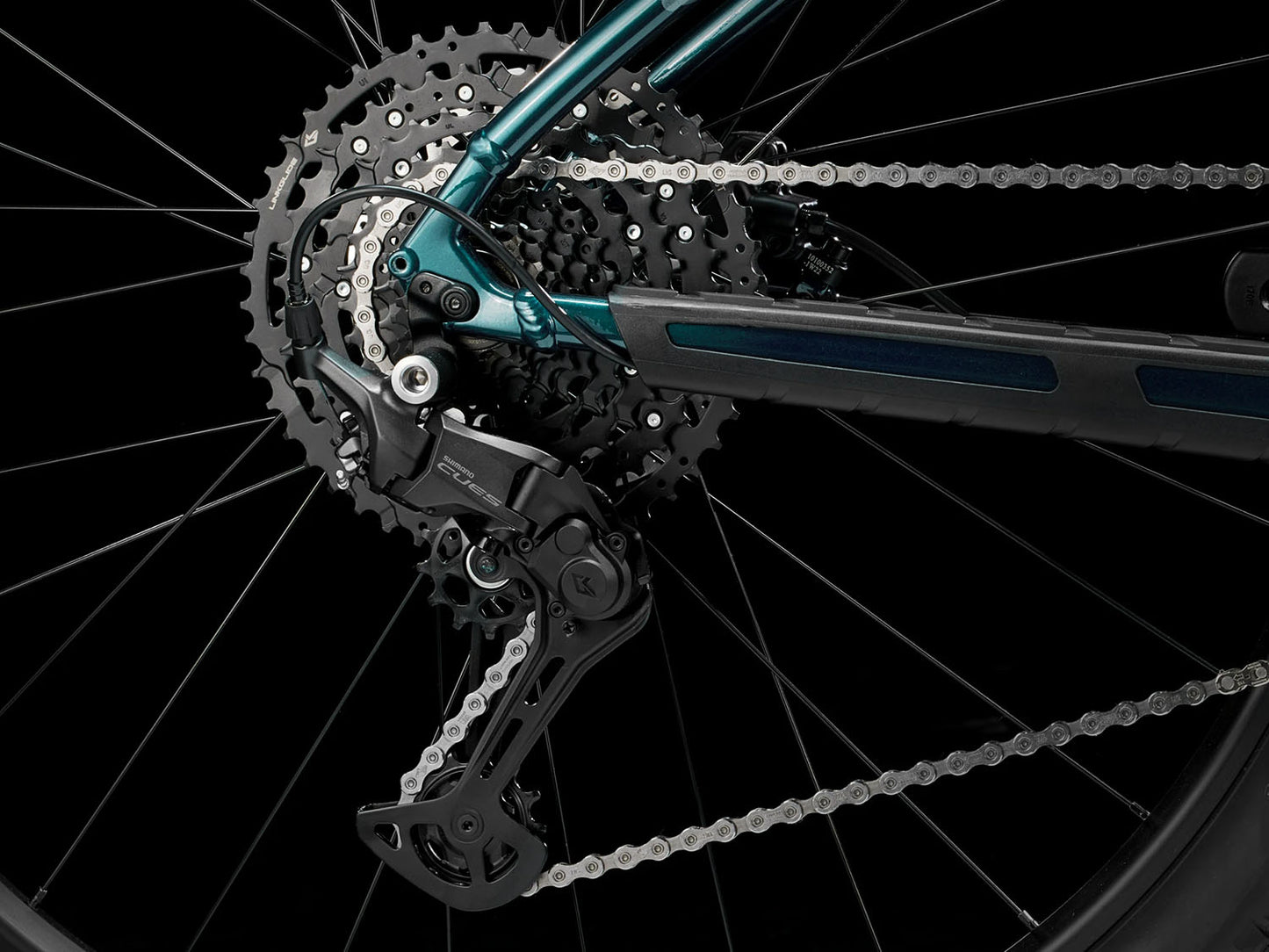 A closeup view of the cassette and rear derailleur of the Trek Marlin 6 Gen 3 mountain bike in Miami Green to Dark Aquatic Fade against a black background.
