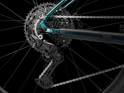 A closeup view of the cassette and rear derailleur of the Trek Marlin 6 Gen 3 mountain bike in Miami Green to Dark Aquatic Fade against a black background.