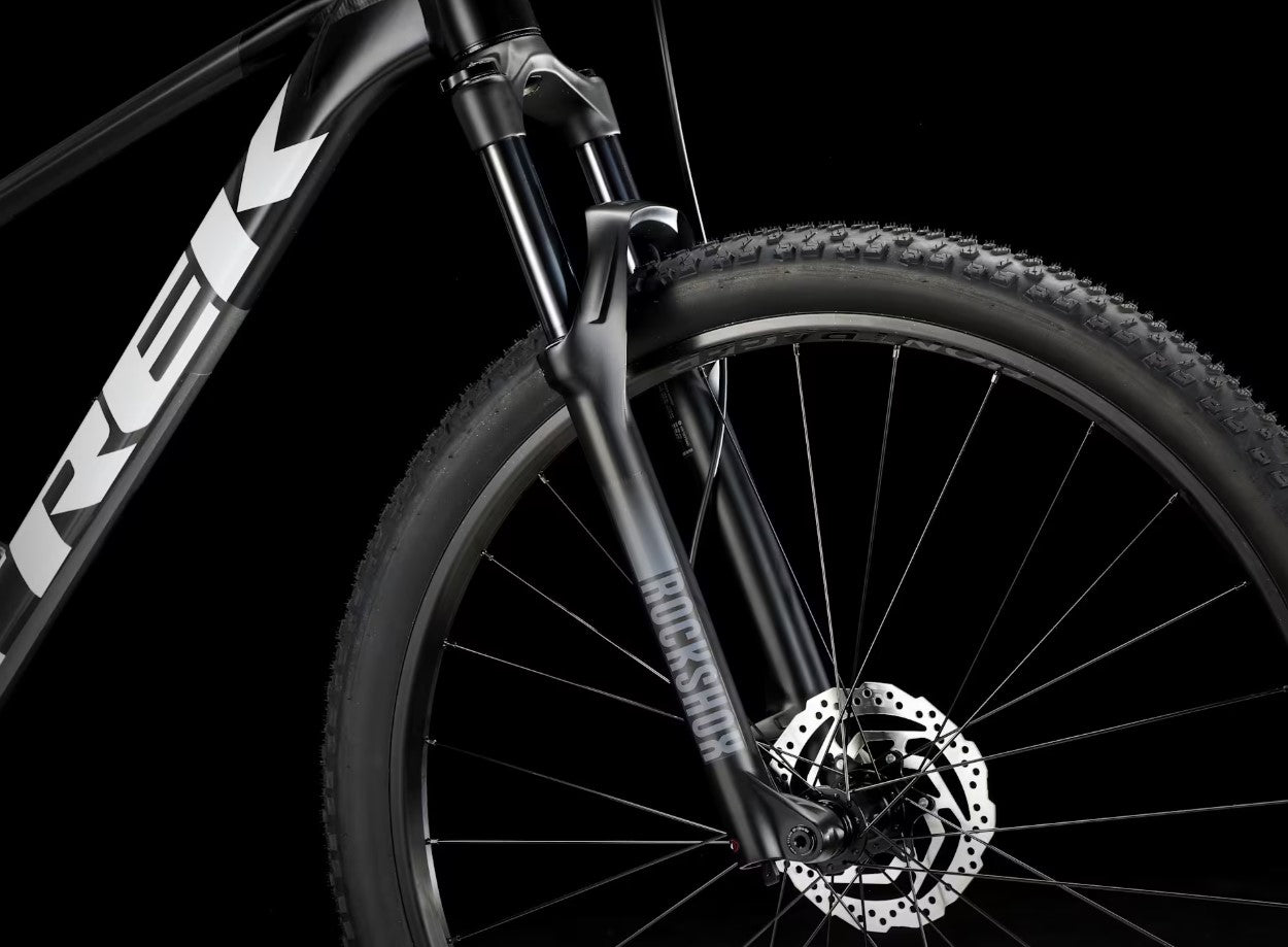 Close-up of a  black Trek Procaliber 6 bicycle's front wheel wheel with disc brake on a black background, featuring the Trek brand.