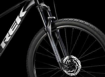 Close-up of a  black Trek Procaliber 6 bicycle's front wheel wheel with disc brake on a black background, featuring the Trek brand.