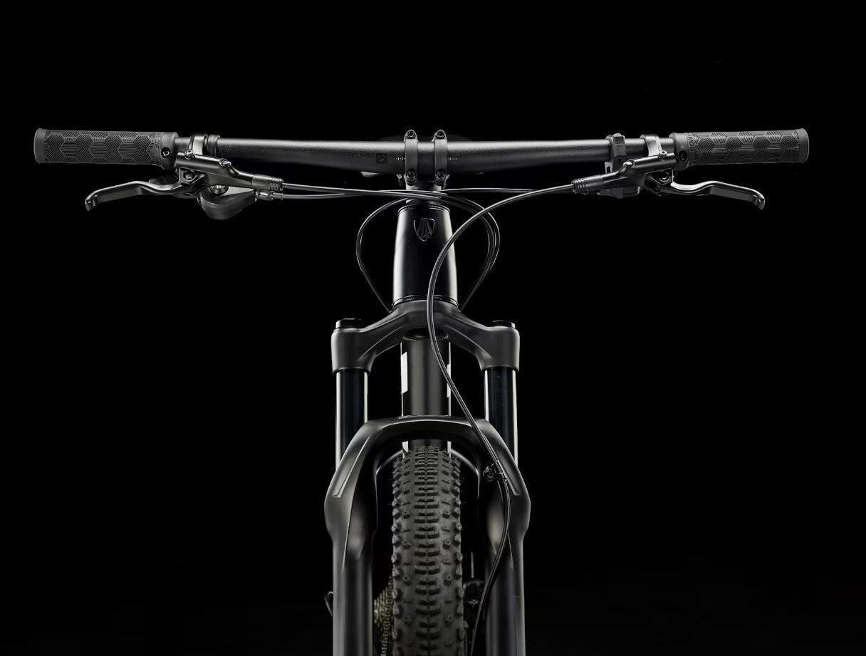 Black Trek Procaliber 6 bicycle with handlebars and front wheel on a black background.
