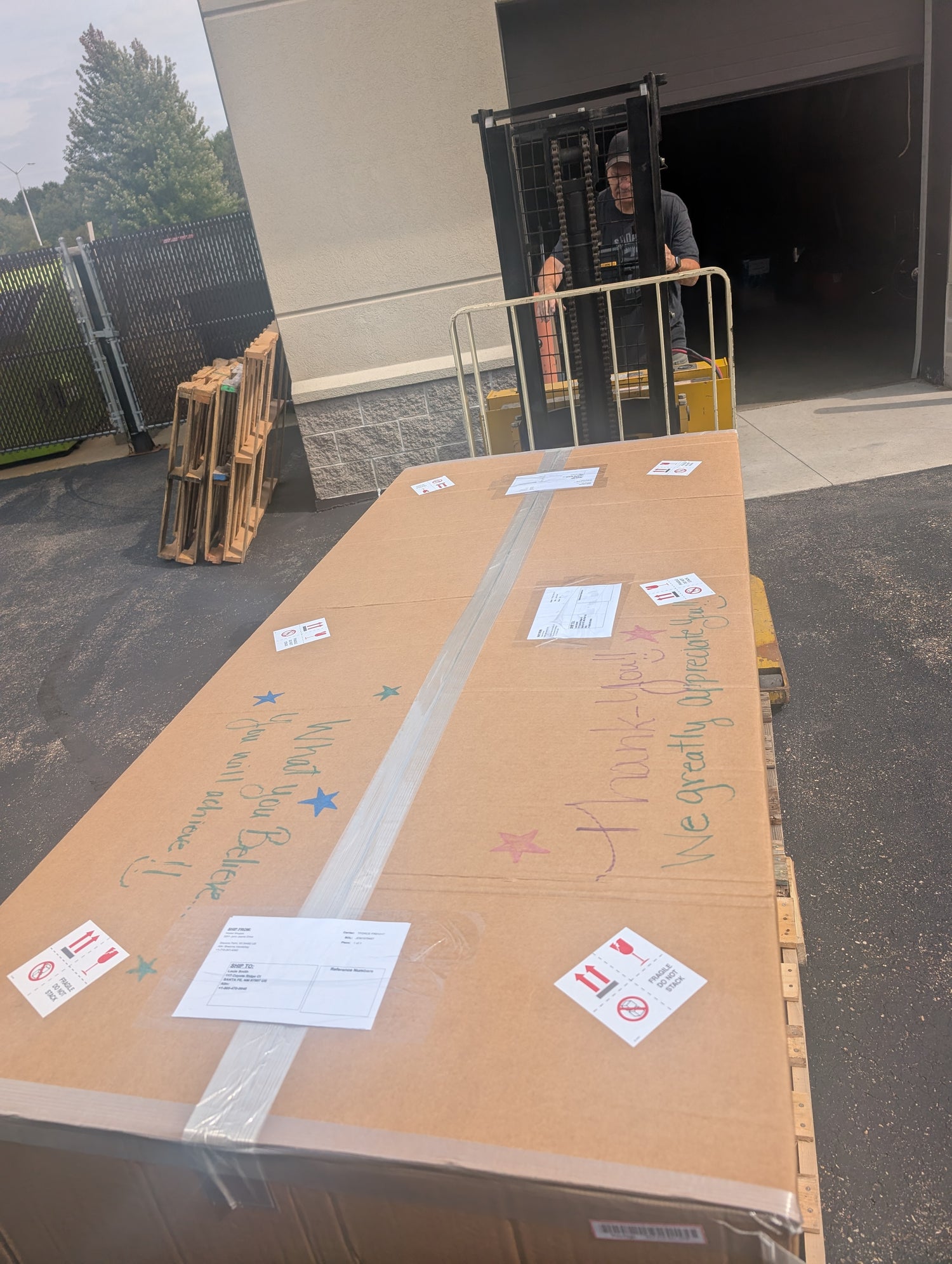 Large cardboard box with labels on a pallet in front of a building entrance.