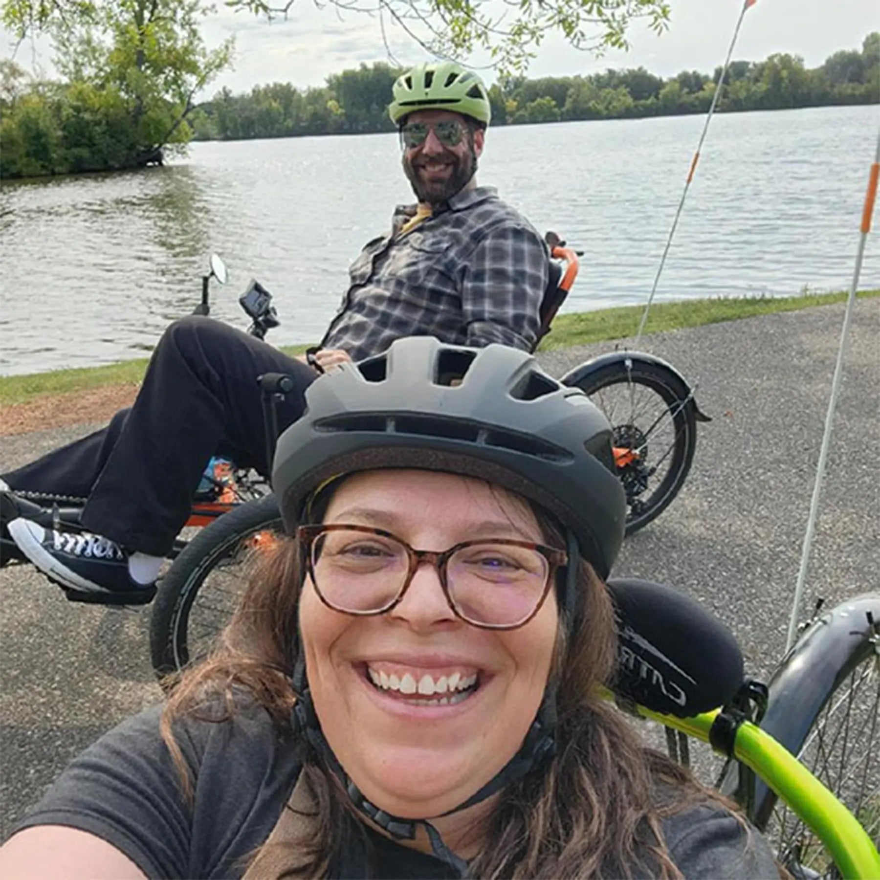 Two people on recumbent trikes by the Wisconsin River with trees in the background.