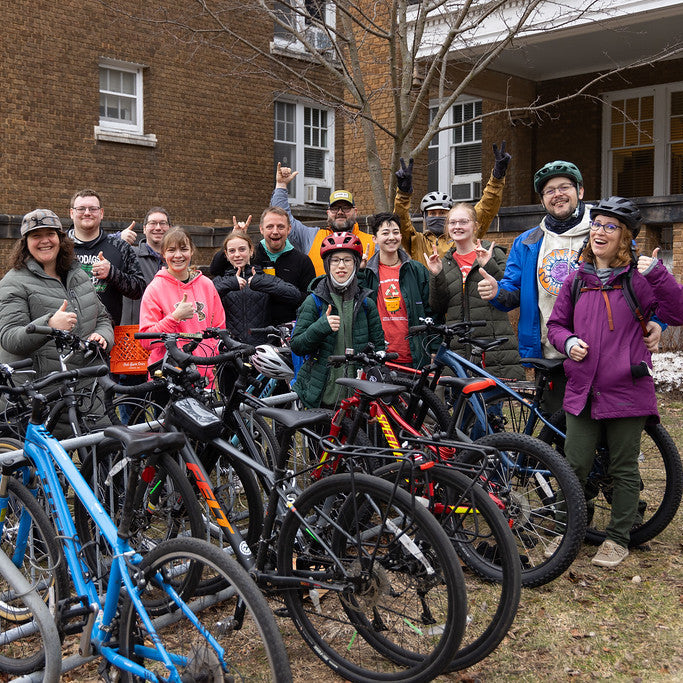 A group of cyclists at the University of Wisconsin-Stevens Point pose with multiple bicycles in front of a brick building. 