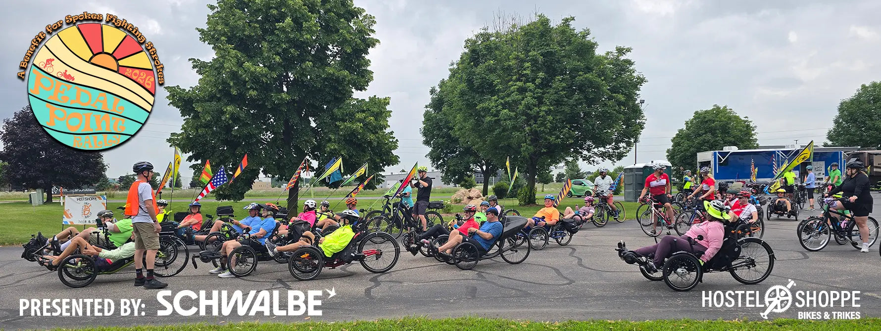 Riders get ready to participate in the Pedal Point Rally bike tour on a cloudy day in 2025. A colorful 2026 Pedal Point Rally logo is in the upper left corner and the Schwalbe and Hostel Shoppe logos are along the bottom.