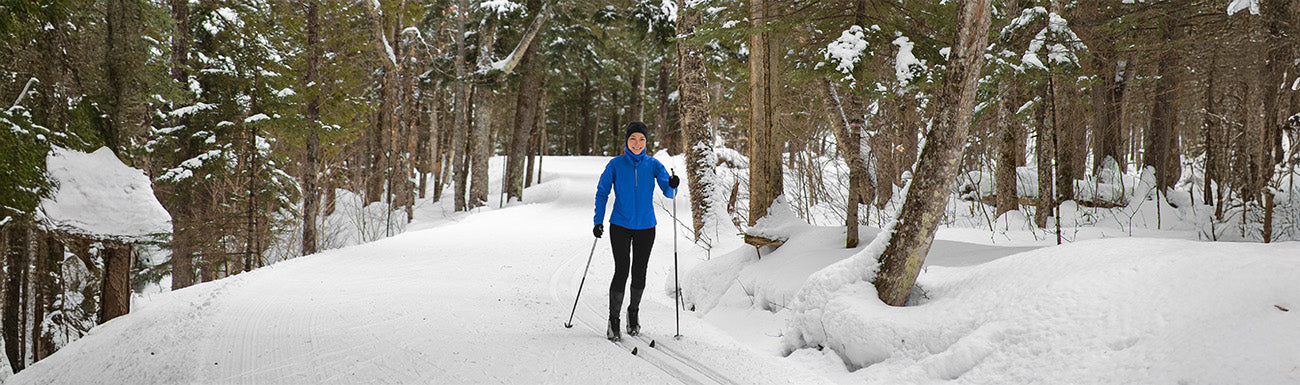 A woman cross-country skiing through a snowy forest.