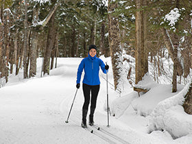 A woman cross-country skiing through a snowy forest.