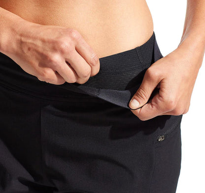 A pair of black Pearl Izumi women's cycling shorts with a wide stretch waistband and hand pockets on a model