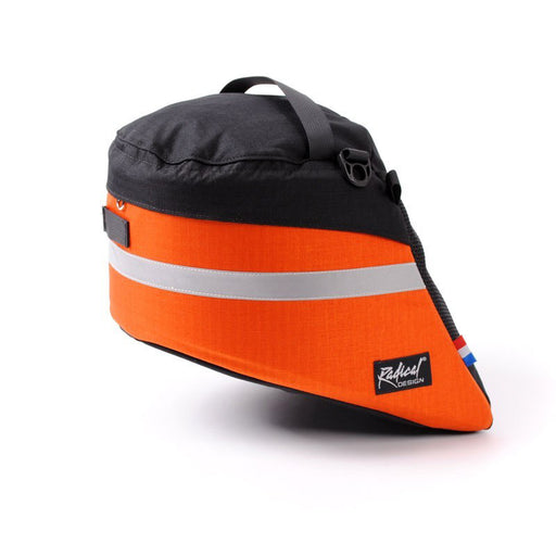 Side view of an orange and black Radical Design Solo Aero Wide recumbent bike bag.  Top of bag is black with a black nylon strap, the main body of the bag is orange with a reflective stripe across it.
