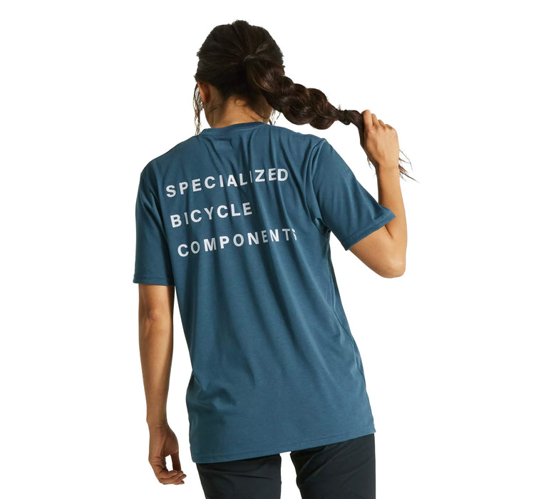 Back view of long-haired model wearing dark blue t-shirt with white lettering across three rows across top half of the shirt. Top row says Specialized, middle row says Bicycle, bottom row says Components