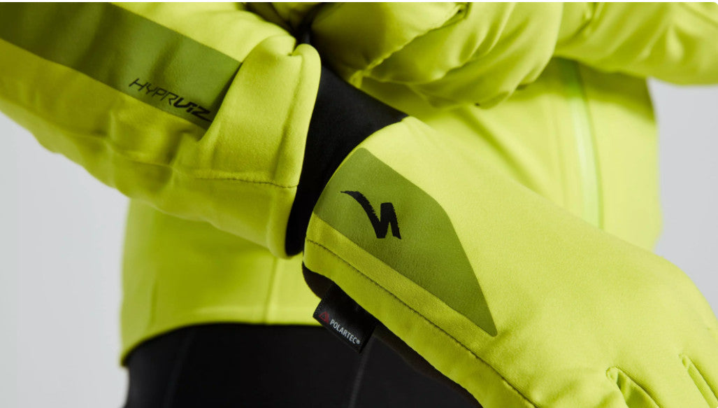 Close up image of model putting on neon yellow Specialized rain gloves with a small black Specialized logo near the cuff below on the smallest finger. 