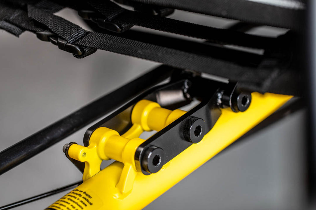 Close up view of black seat extender under a seat, attached to a yellow frame.