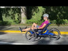 Woman in purple t-shirt and white helmet riding a bright blue recumbent trike along the road