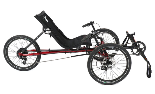 Side view of a red and black TerraTrike Traveler recumbent trike with a black seat and folding handlebars, equipped with a chain drive and mechanical disc brakes.